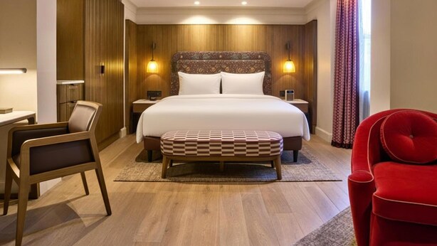 Una habitació d'hotel amb un llit gran, taules de nit, un escriptori, una cadira i un butacó vermell.