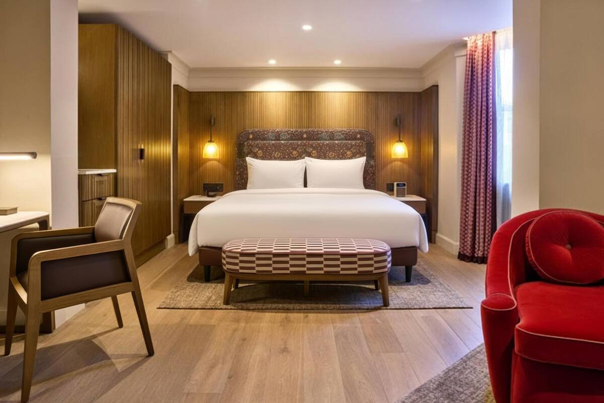 A hotel room with a large bed, bedside tables, a desk, a chair, and a red armchair.