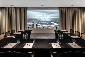 A conference room with a large screen displaying the Edwardian Hotels London logo, a long table with chairs, water bottles, and glasses. - Radisson Blu Hotel, London Mercer Street (London)
