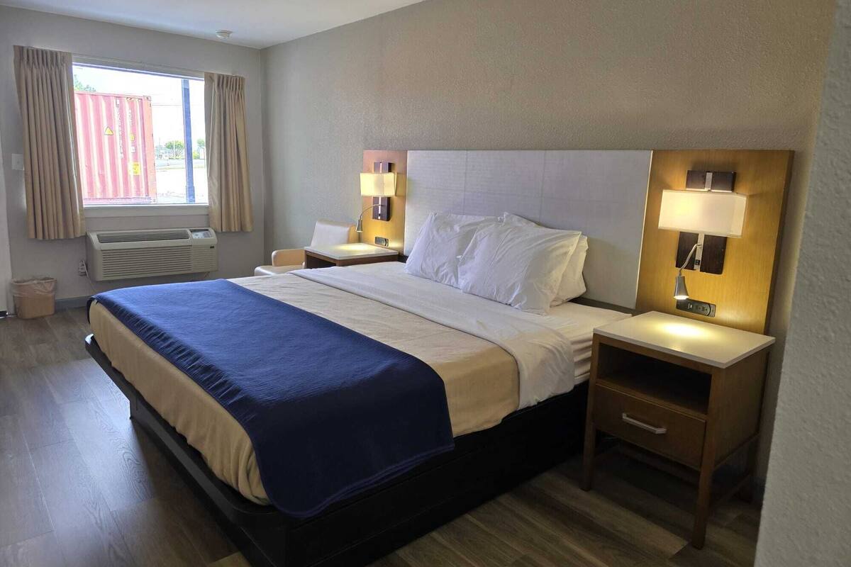 Habitación de hotel con una cama grande, dos mesitas de noche con lámparas, una ventana con cortinas y un equipo de aire acondicionado.