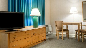 A hotel room with a television on a wooden dresser, a desk with two chairs, a lamp, and a large window with blue curtains. - Econo Lodge South (Buffalo)