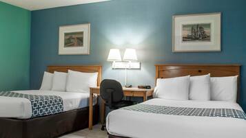 A hotel room with two beds, a desk with a chair, two wall-mounted lamps, and two framed pictures on the walls.