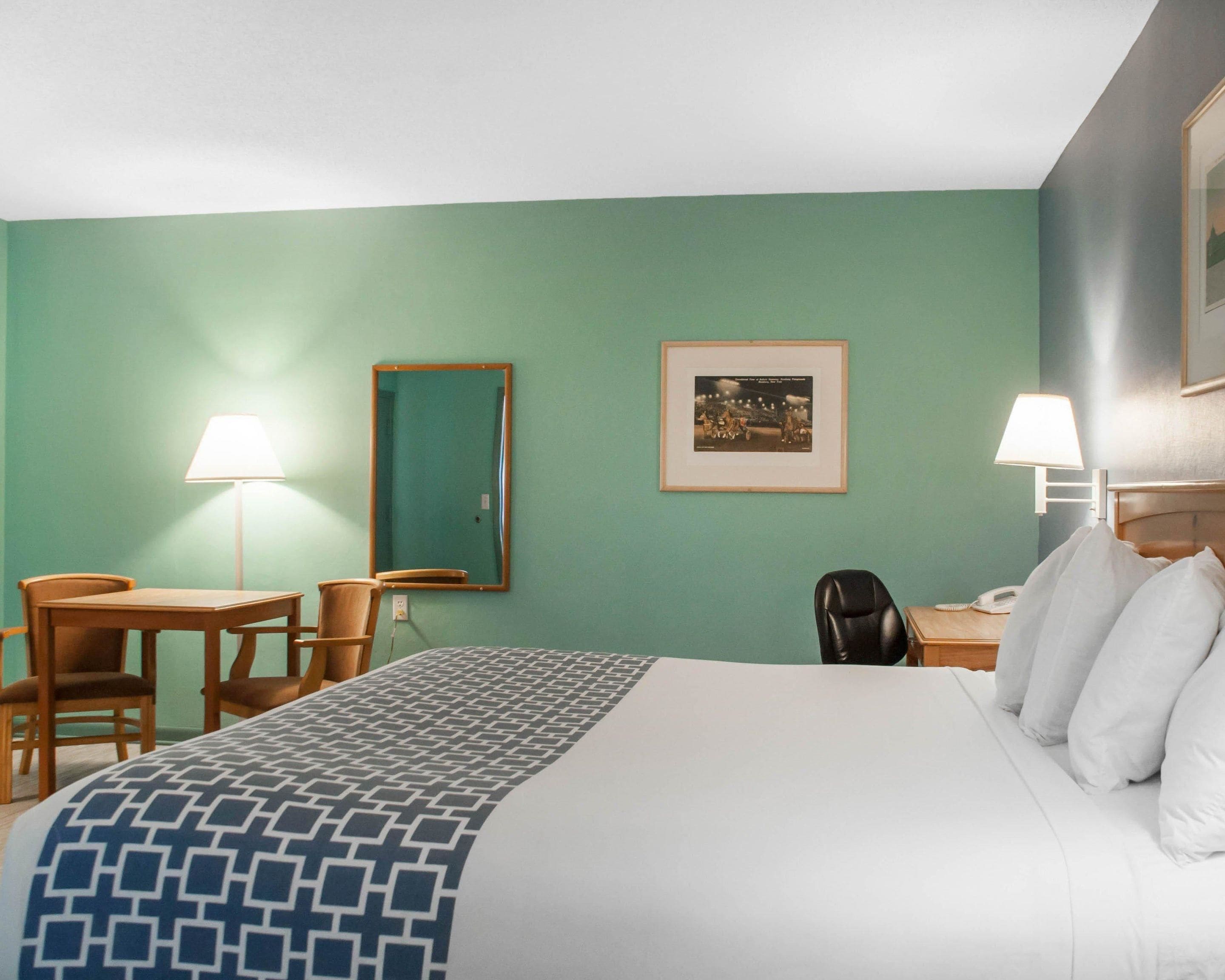 A hotel room with a bed, two chairs, a desk, a mirror, and a framed picture on the wall.