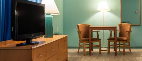 Ein Hotelzimmer mit Fernseher auf einer Holzkommode, zwei Stühle um einen kleinen Tisch und zwei Lampen.