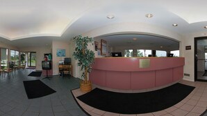 A reception area with a curved pink counter, a television on a stand, a computer, and a large potted plant. - Econo Lodge South (Buffalo)