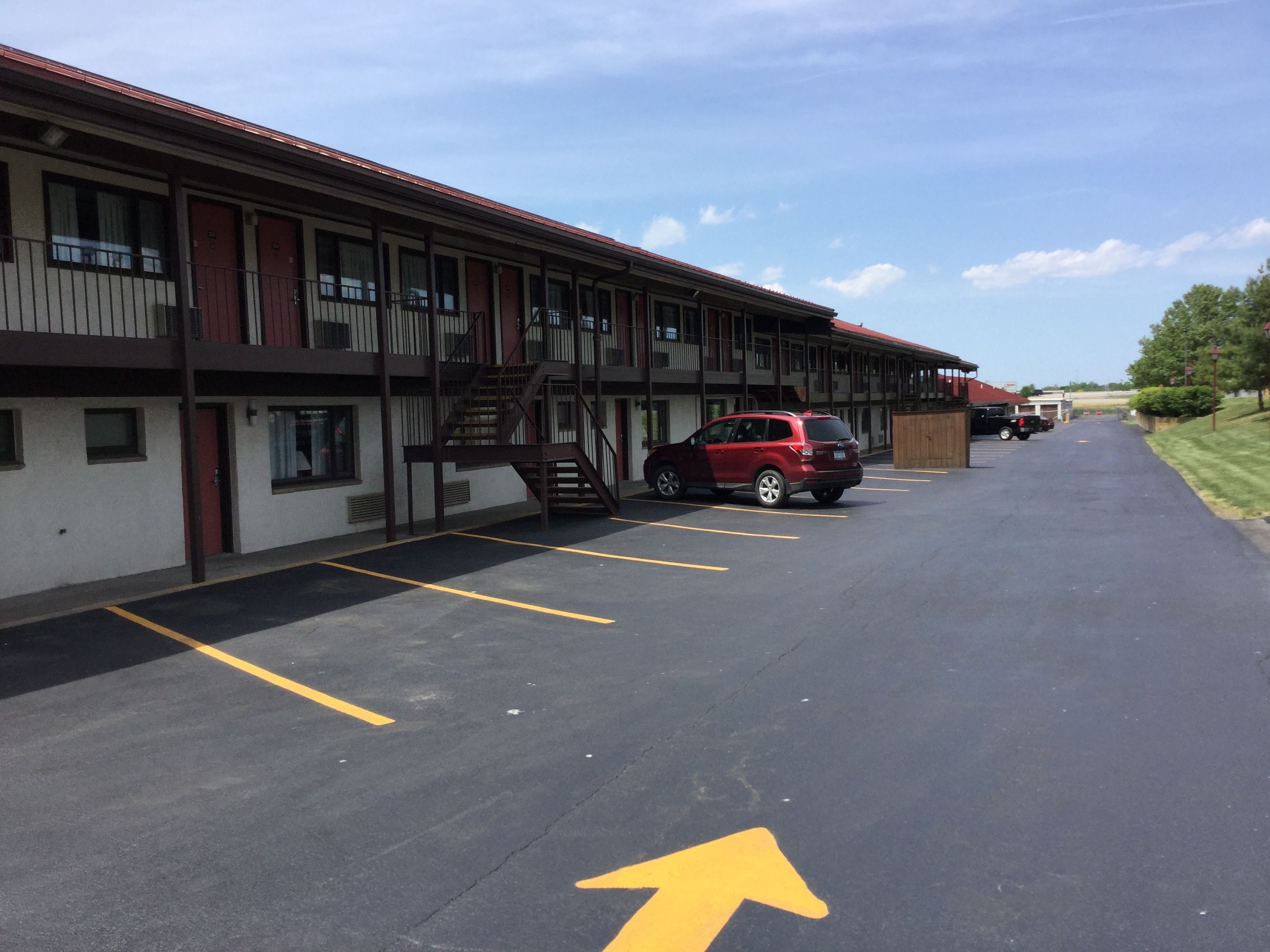 A motel with a parking lot, a red SUV parked in one of the spaces, and a yellow arrow on the ground indicating direction.