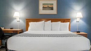 A hotel room with a large bed, two bedside lamps, a desk with a chair, and a framed picture on the wall. - Econo Lodge South (Buffalo)