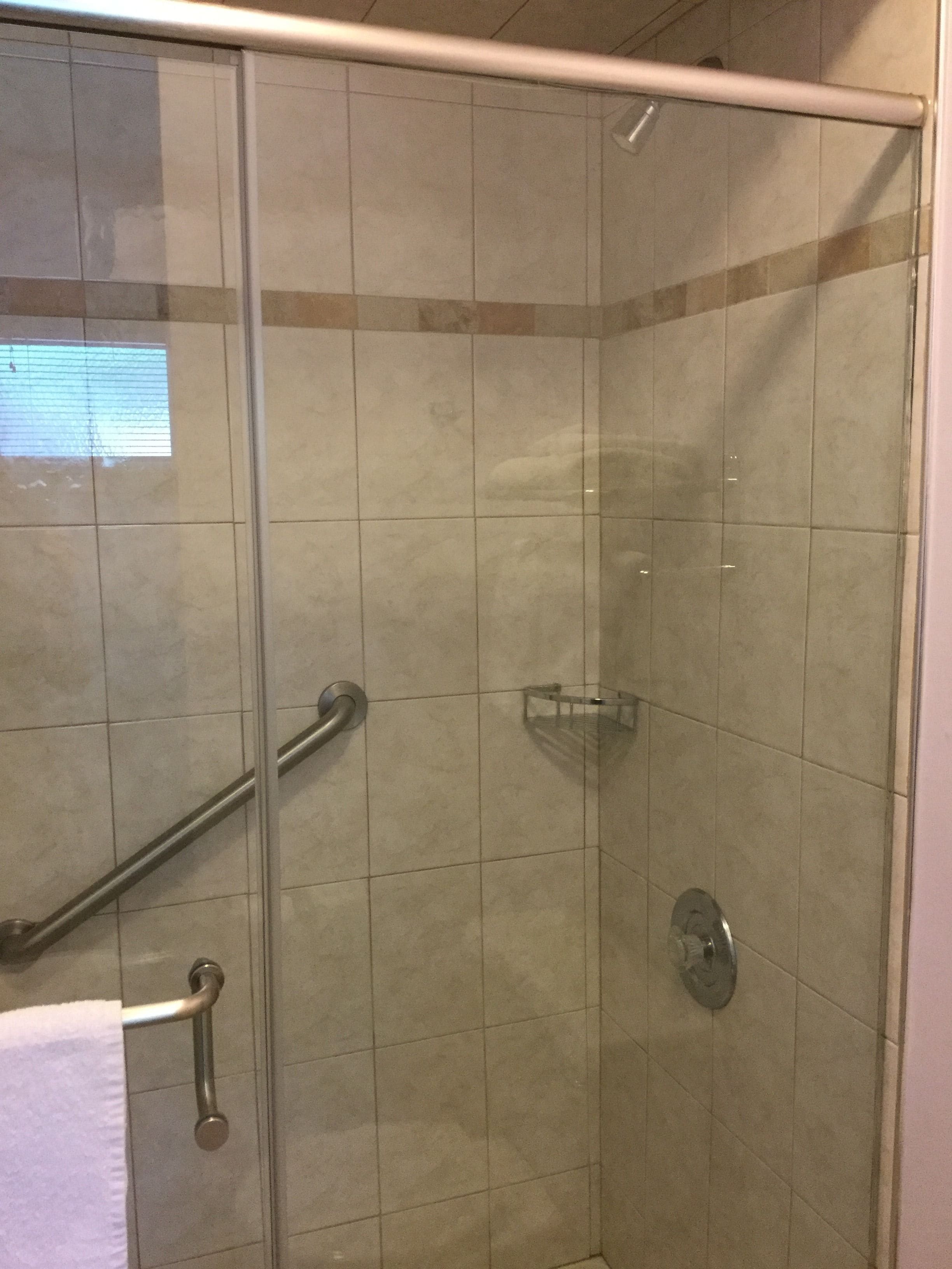 A glass-enclosed shower stall with a handrail, a glass shower door, and a tiled wall.