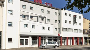 Ein weißes Gebäude mit 'ibis HOTEL'-Beschilderung, zahlreichen Fenstern und einem geparkten Auto davor.