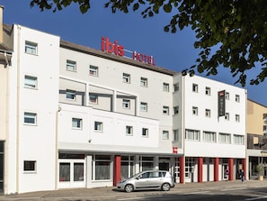 Een wit gebouw met 'ibis HOTEL' bord, meerdere ramen en een auto geparkeerd ervoor.