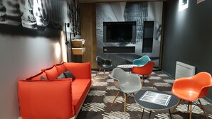 Ein stilvoller Lounge-Bereich mit einem roten Sofa, mehreren Sesseln, einem kleinen Tisch und einem flachbildfernseher an der Wand.