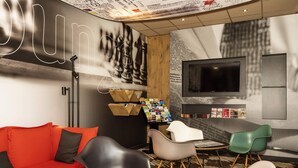Ein stilvoller Lounge-Bereich mit einem roten Sofa, schwarzen und weißen Sesseln, einem kleinen Tisch und einem an der Wand befestigten Fernseher.