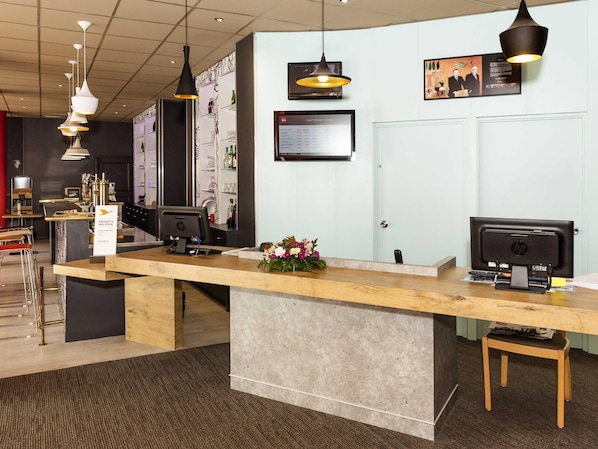 Un comptoir d’accueil avec une signalétique indiquant un service prioritaire, un ordinateur HP et un tableau affichant le menu.