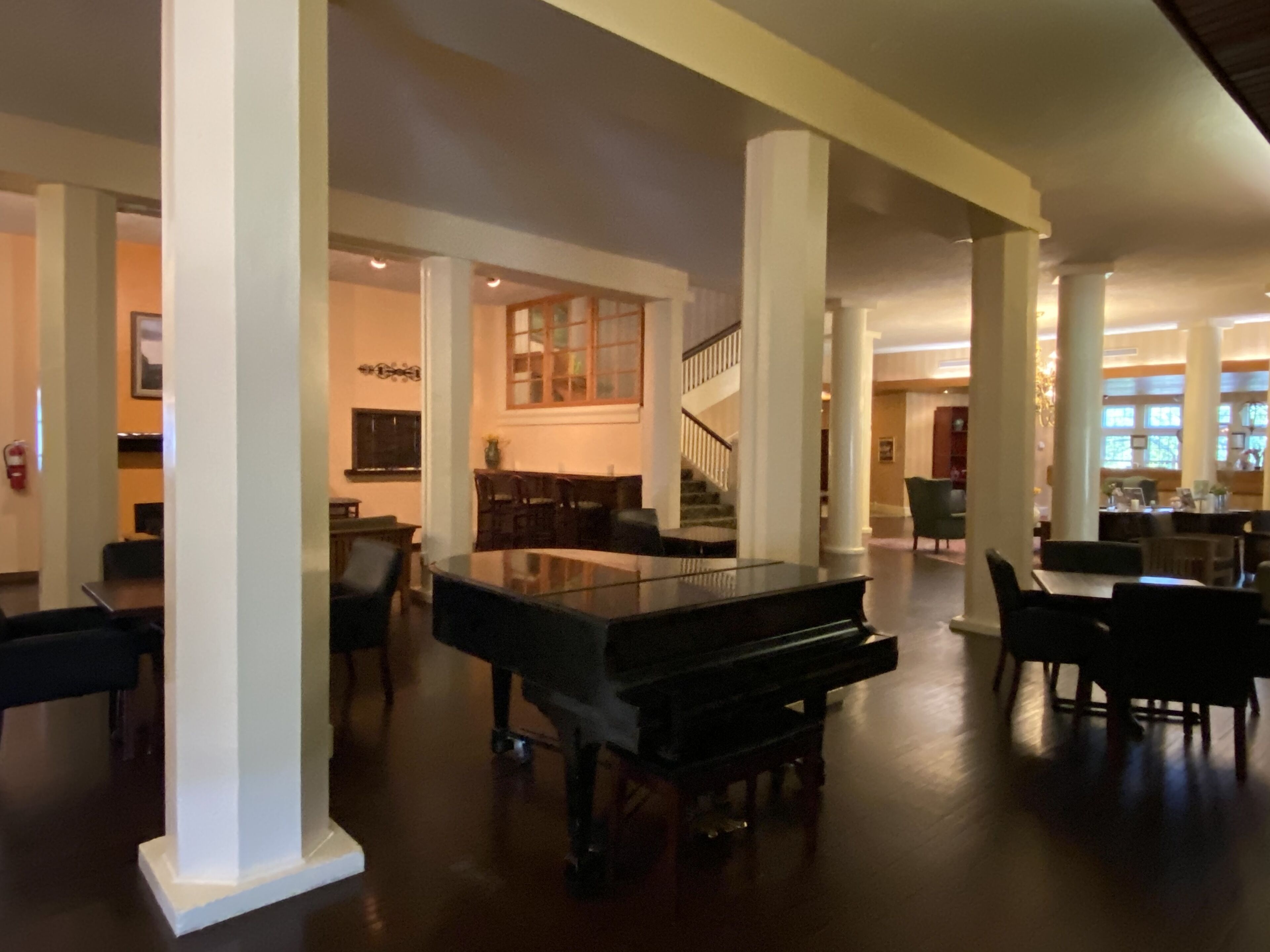 A spacious lobby with a grand piano, high ceilings, and a staircase leading to upper floors.