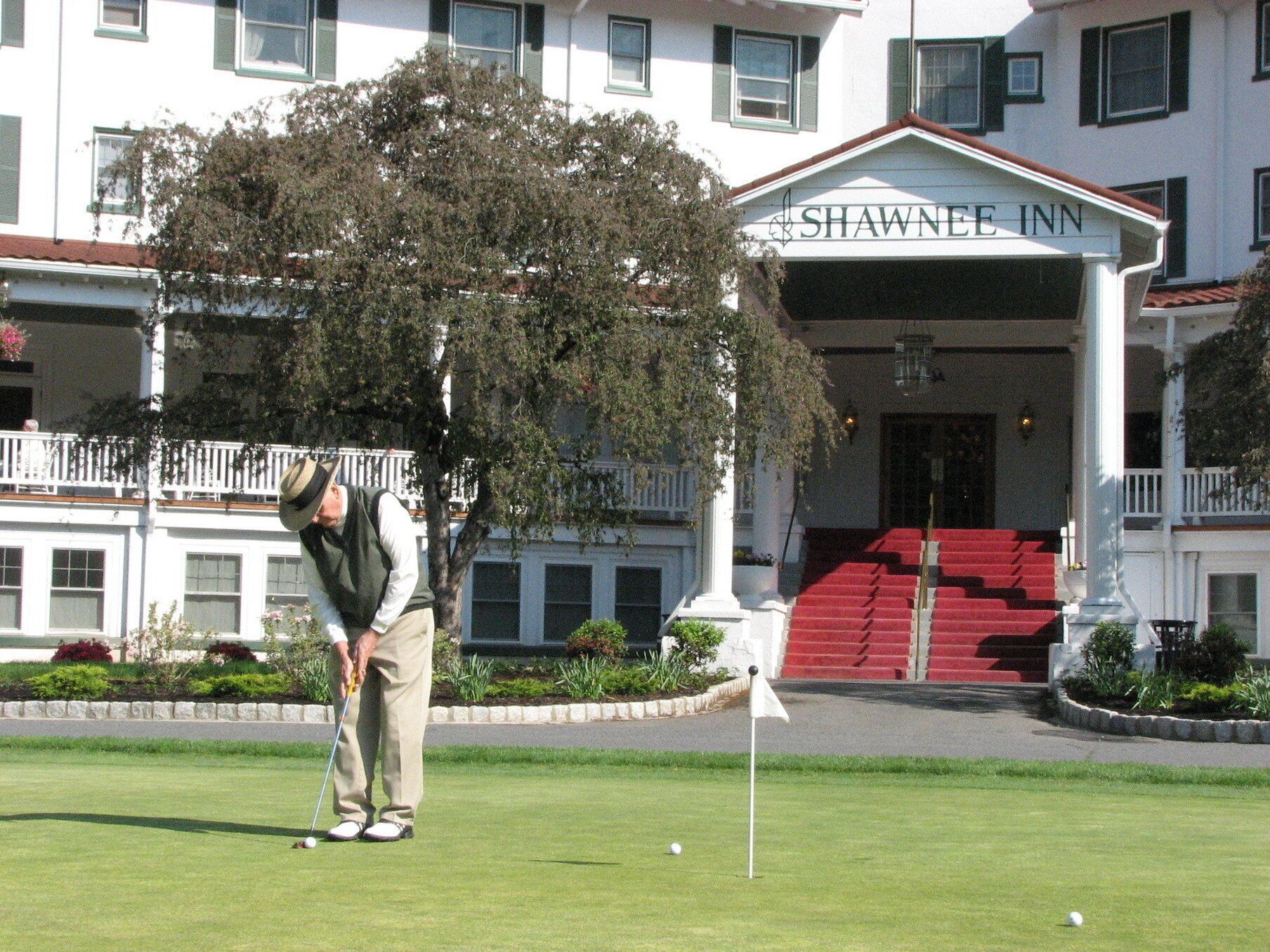 A golf course with a flagstick, a golfer in a green vest, and a building labeled "SHAWNEE INN" in the background.