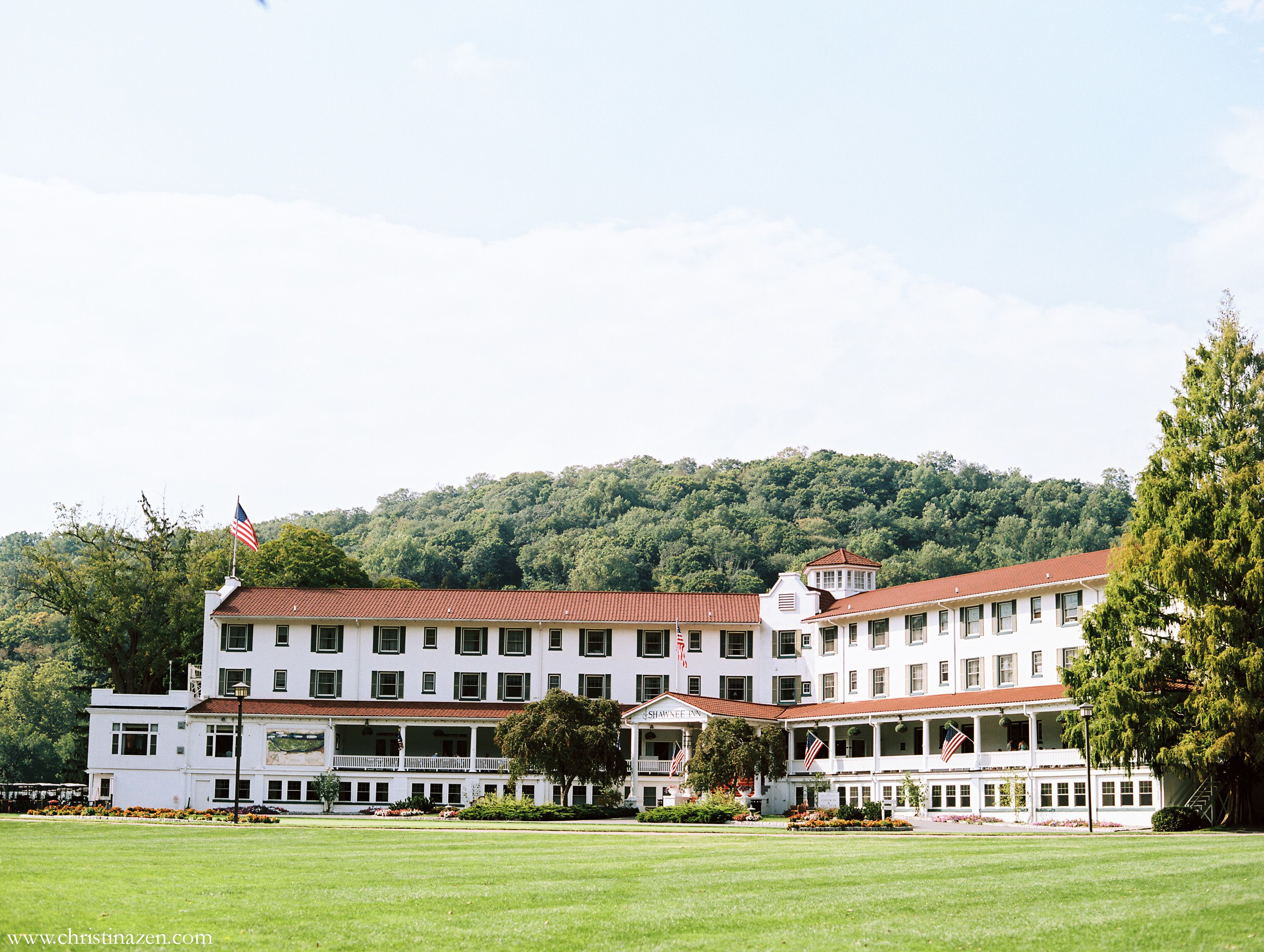 Ein großes, mehrstöckiges Hotel mit rotem Ziegeldach und weißen Außenwänden, umgeben von gepflegten Rasenflächen und Bäumen.