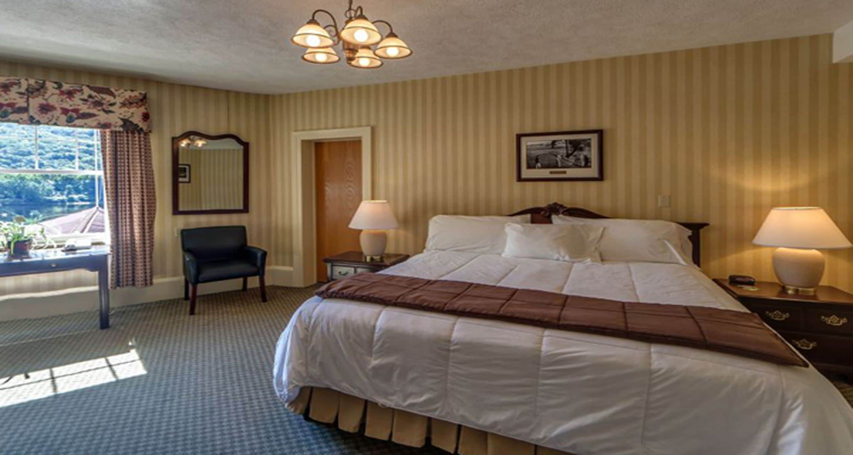 A hotel room with a large bed, two bedside lamps, a chair, a desk, and a window with curtains.