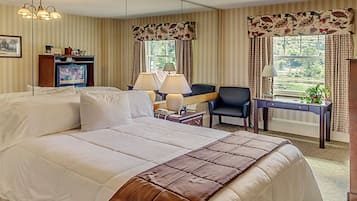Ein Hotelzimmer mit einem großen Bett, einem Schreibtisch, zwei Stühlen, einem Fernseher und einem Fenster mit Vorhängen.