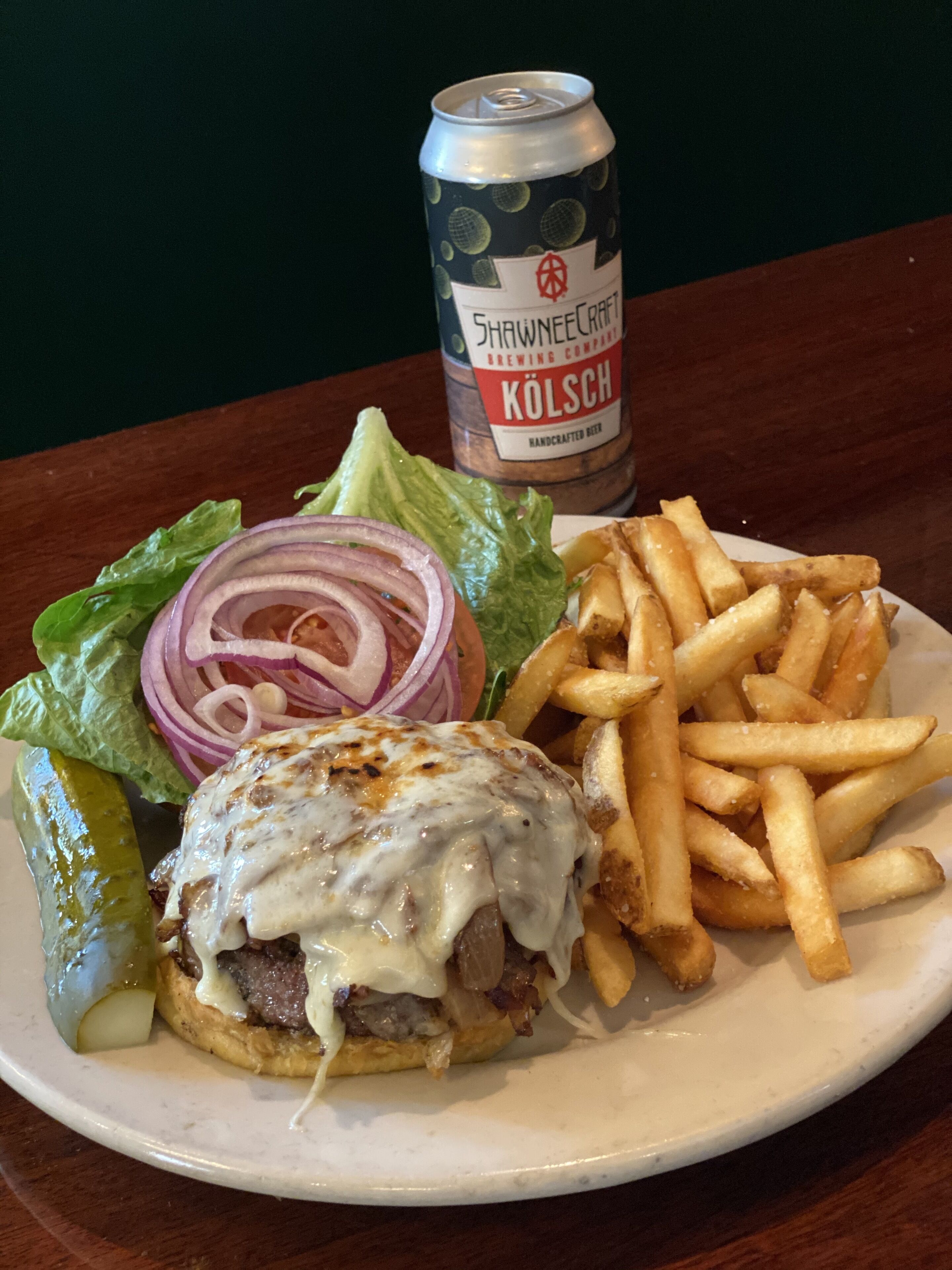 A plate with a burger, fries, a pickle, and a can of beer.