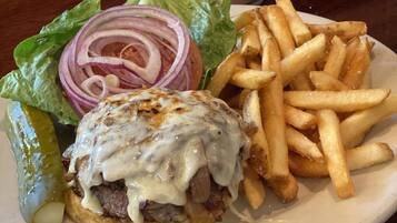 A plate with a burger, fries, a pickle, and a can of beer.