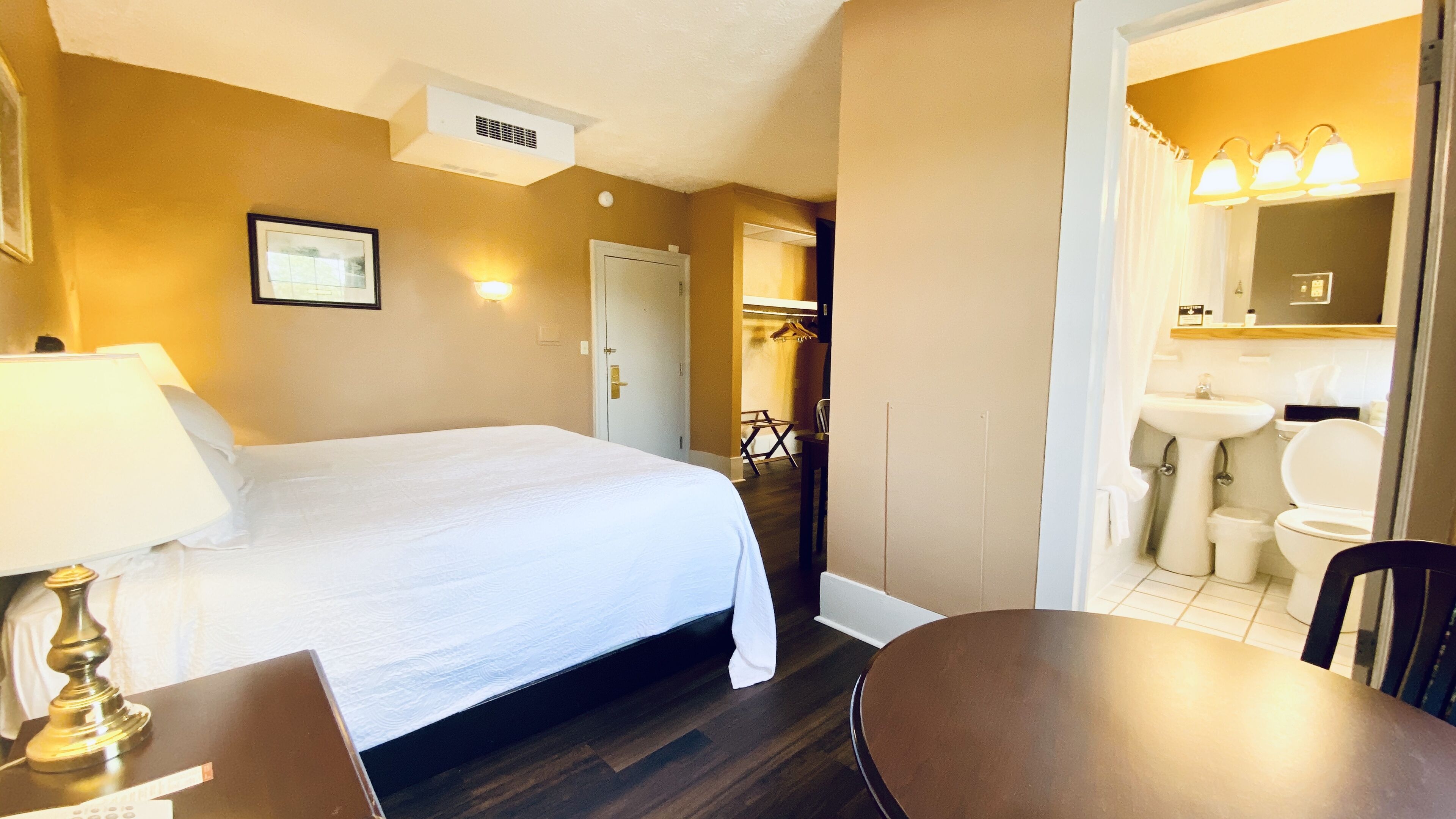 A hotel room with a bed, a desk, a chair, a bathroom with a sink and toilet, and a coat rack.