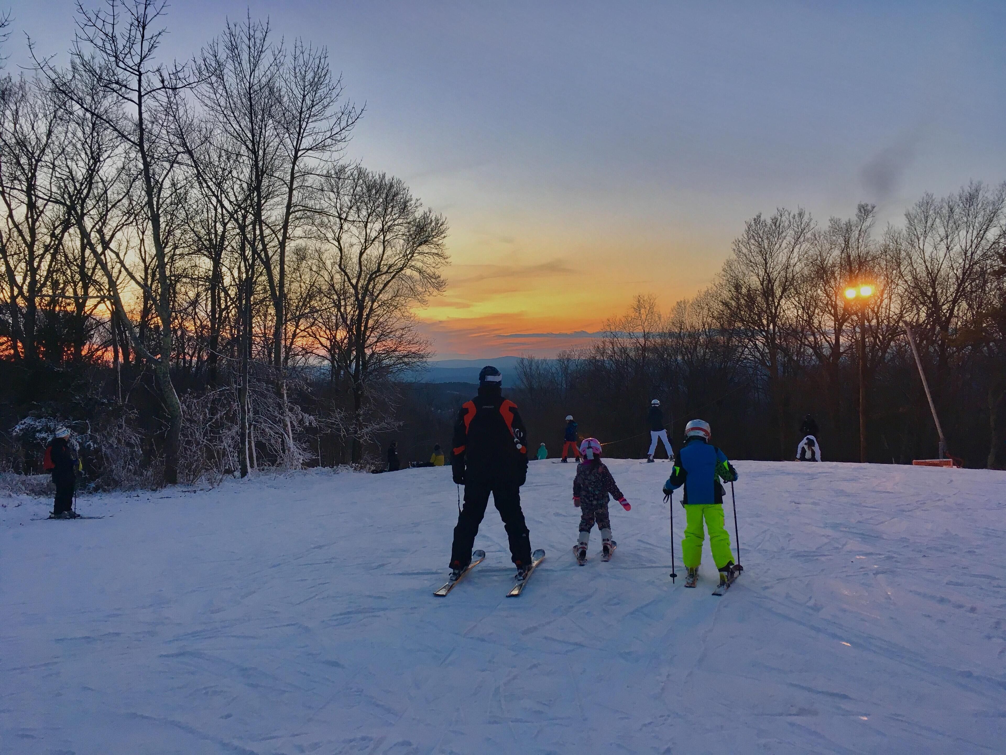 A snowy landscape with skiers and a sunset in the background.