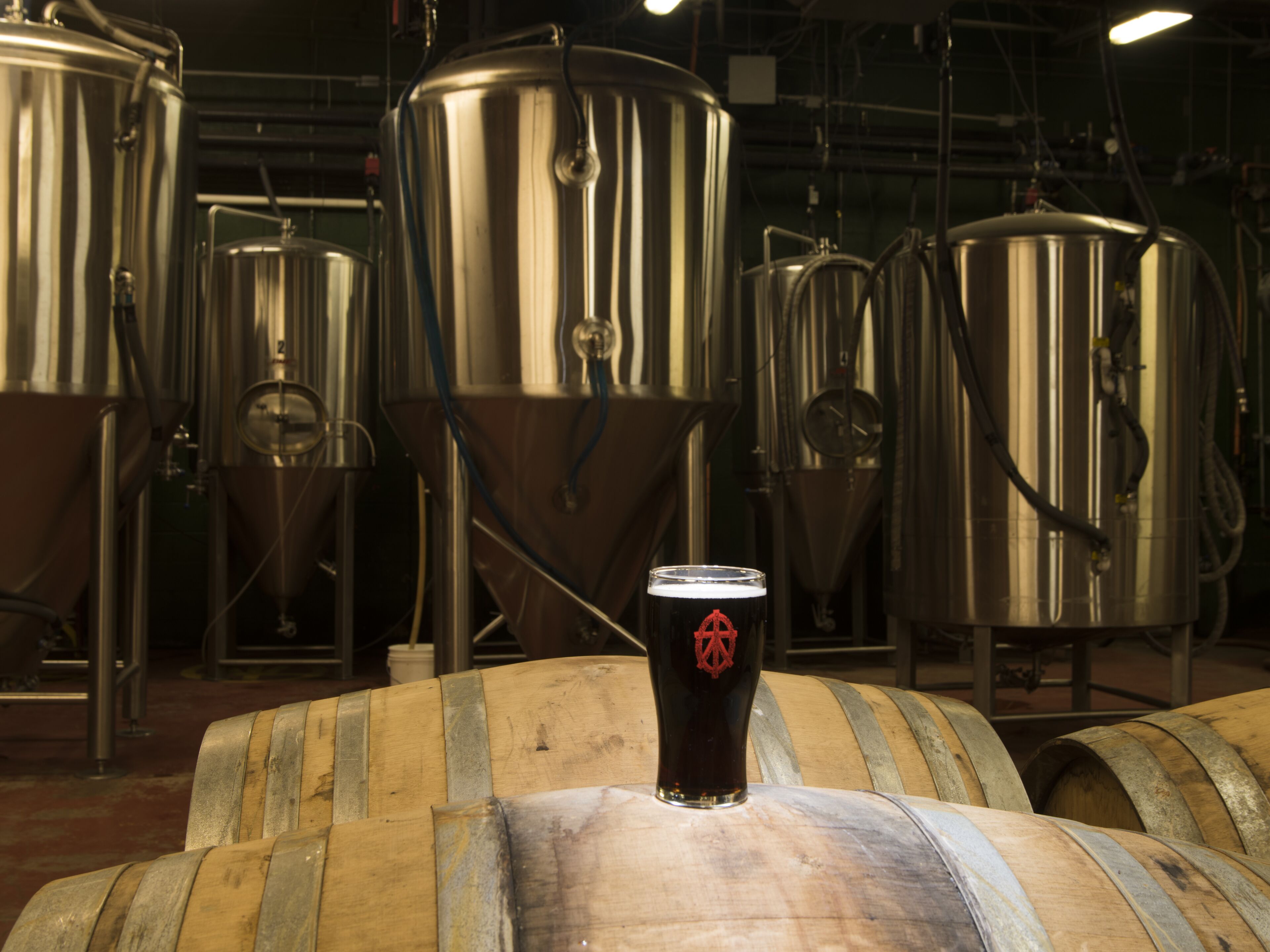 Stainless steel brewing tanks and wooden barrels in a brewery setting.