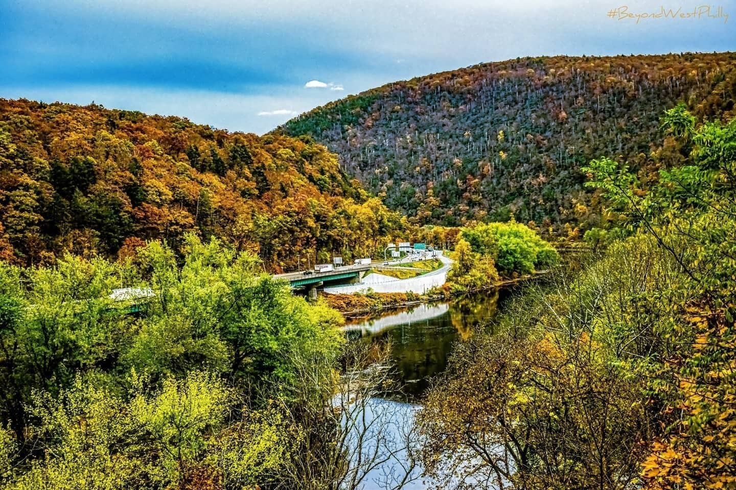 Un río con un puente, rodeado de árboles y colinas de colores otoñales.