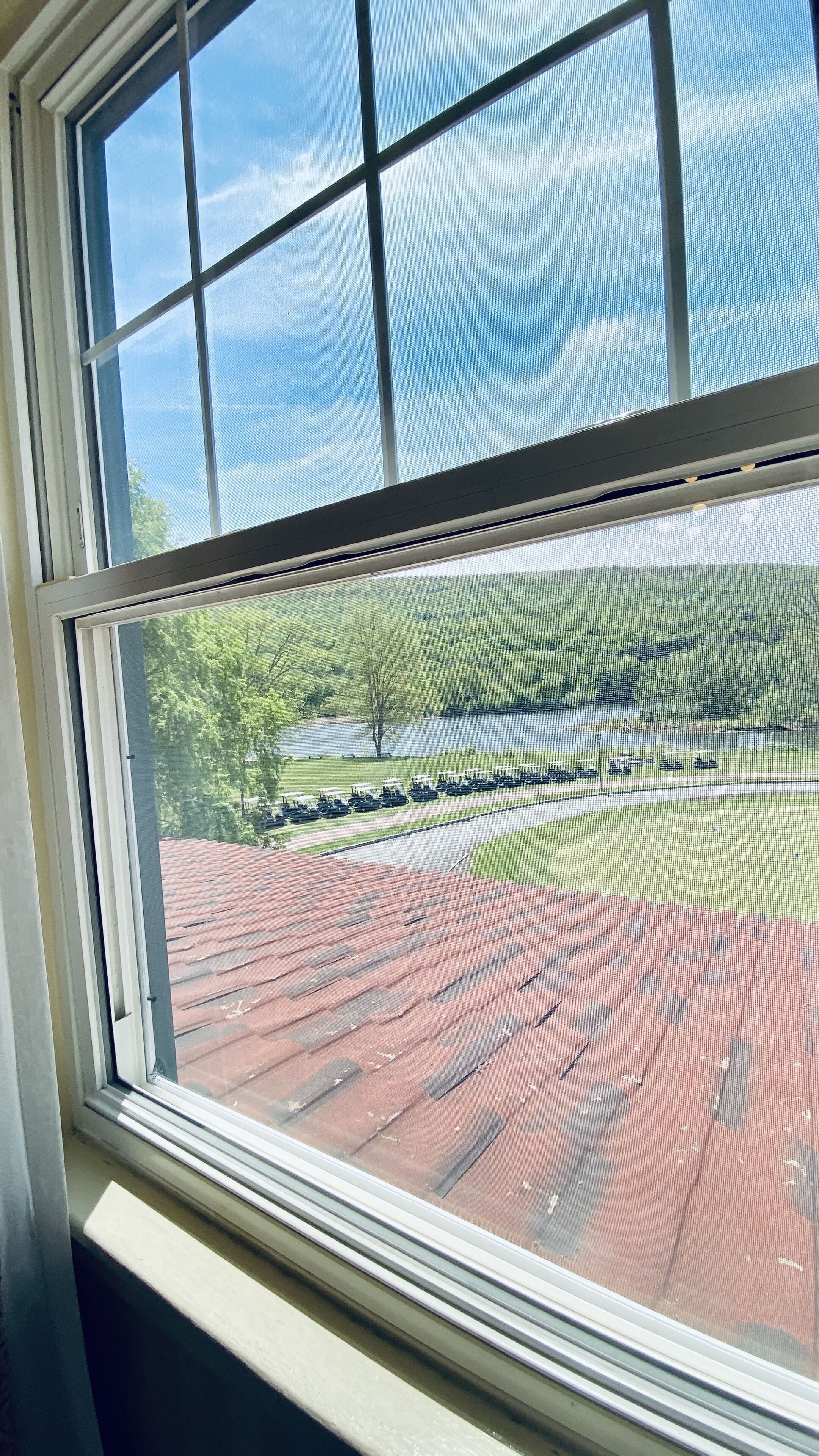A window with a view of a parking lot with golf carts and a building with a red roof.