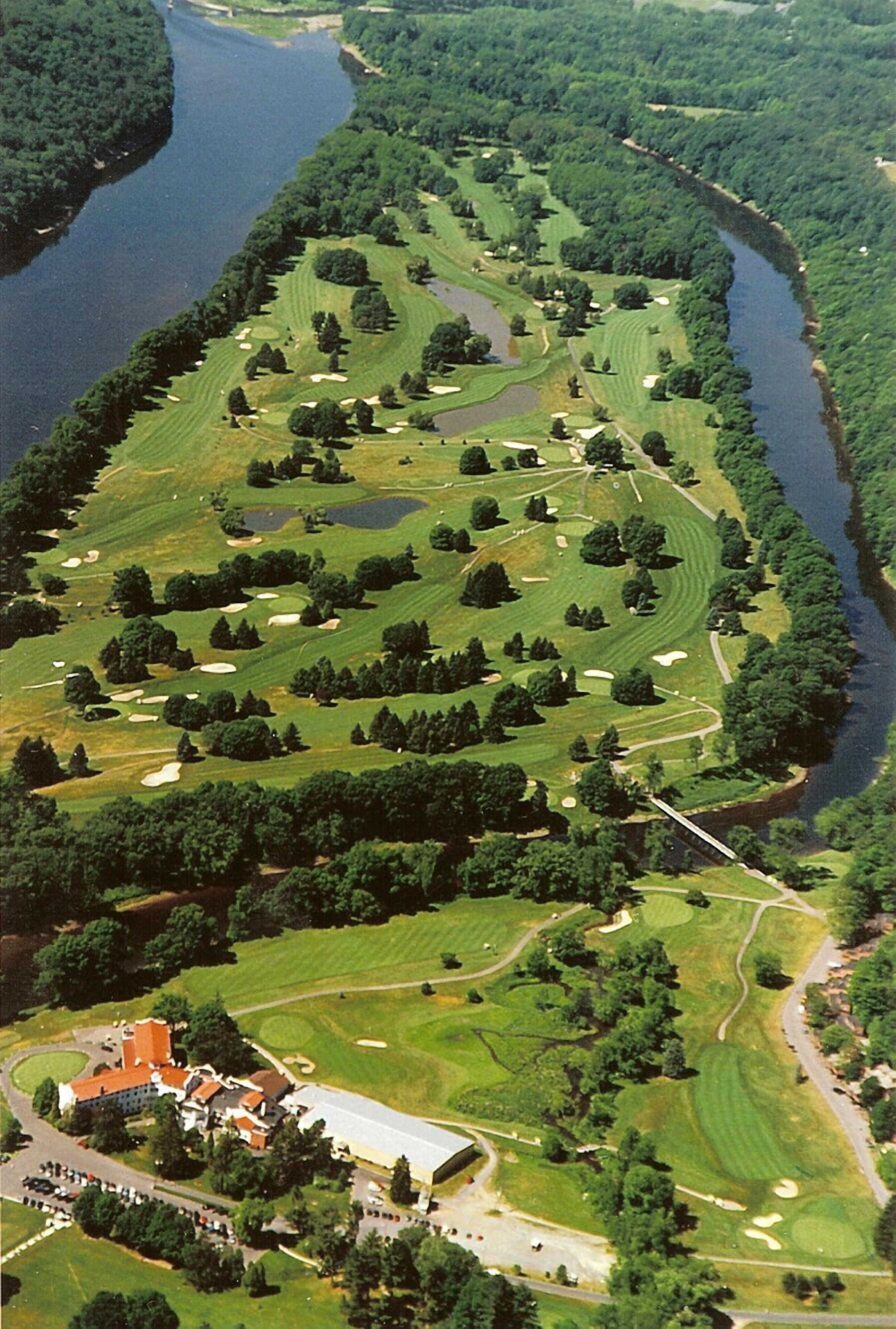 Oversigtsbillede af en golfbane med en flod langs den ene side og en bygningkompleks i bunden.