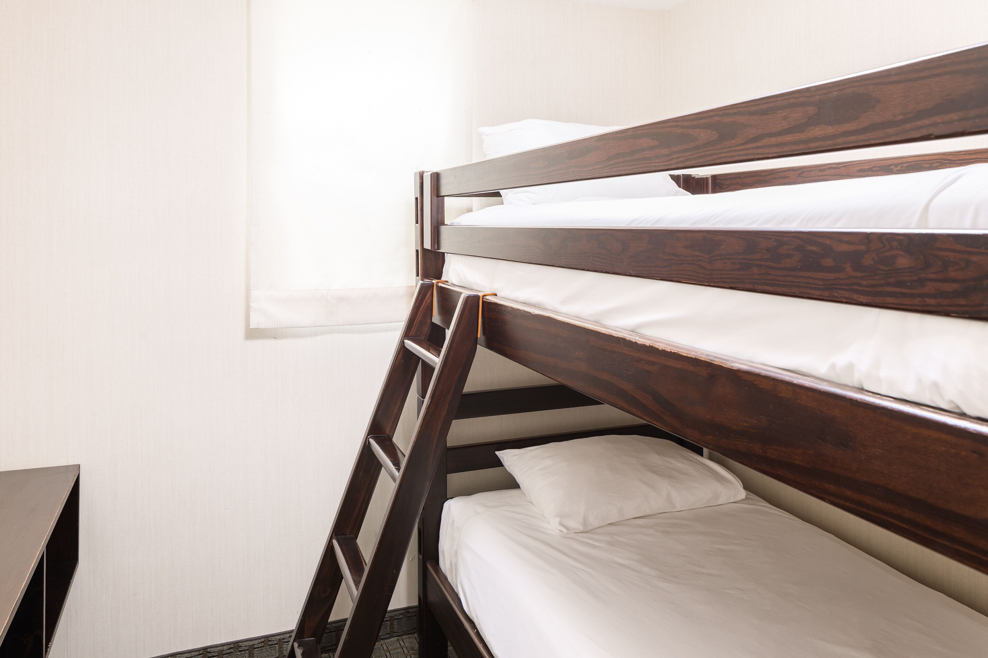 Un letto a castello con testiere in legno e biancheria bianca in una stanza dalle pareti spoglie.