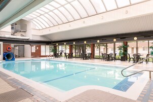 An indoor swimming pool with a glass ceiling, surrounded by tables and chairs, and a lifebuoy near the pool's edge.