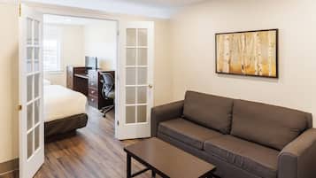 A room with a bed, a brown sofa, a wooden coffee table, a desk with a chair, and a painting on the wall.