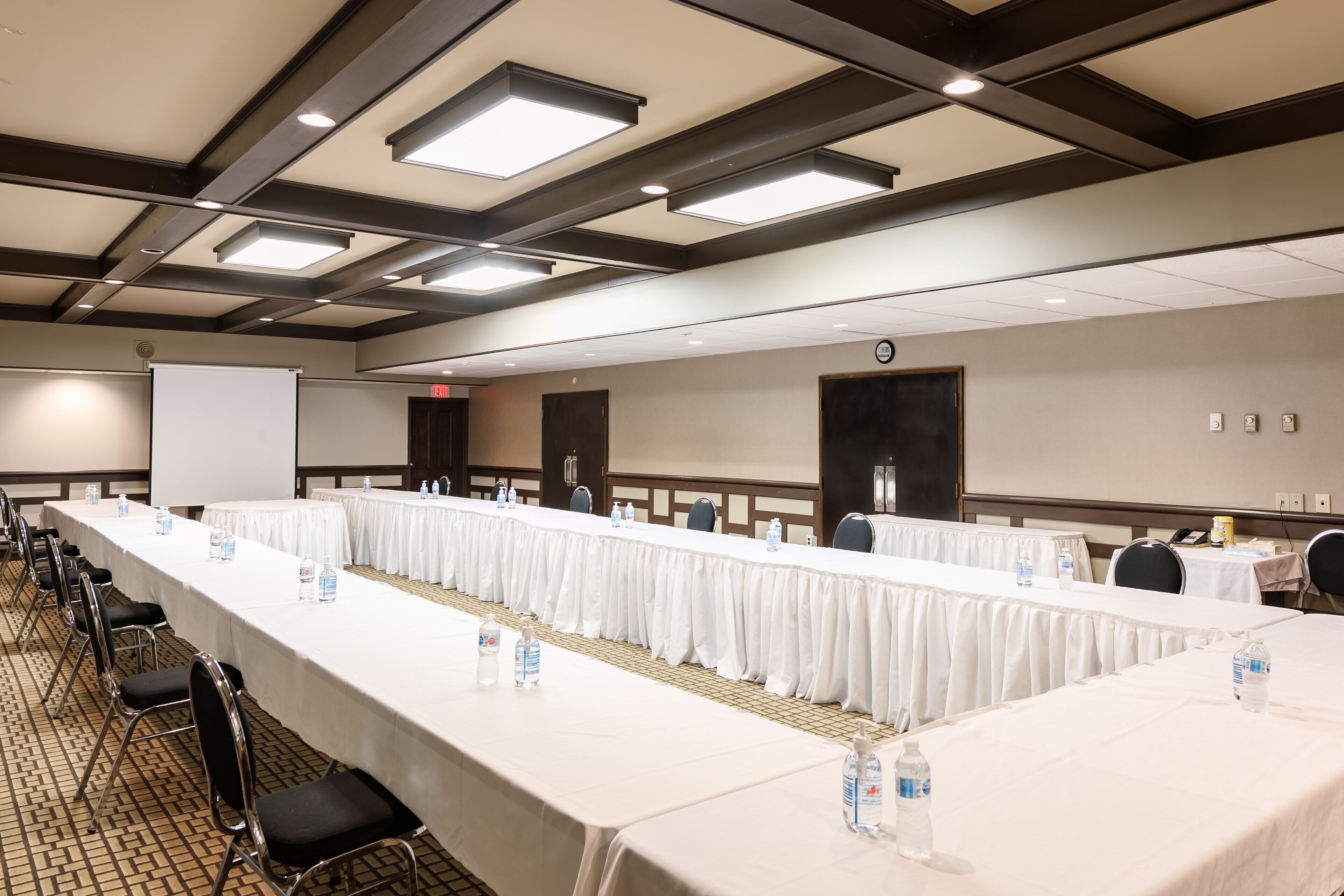 A conference room with long tables, chairs, and a projector screen.