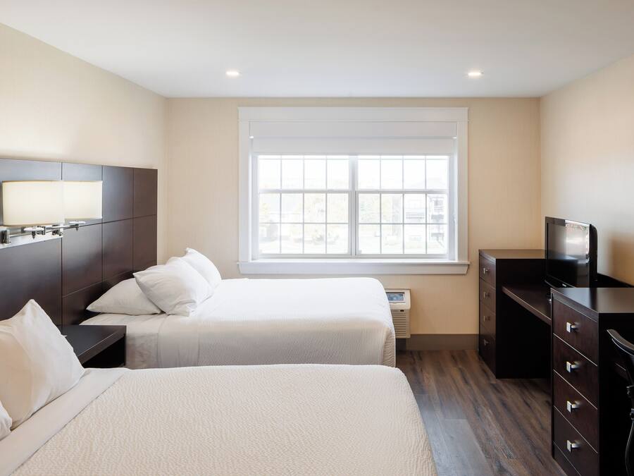 A hotel room with two beds, a TV, a dresser, and a window with blinds.