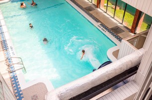 A swimming pool with clear blue water, a tiled deck, and a glass balustrade.