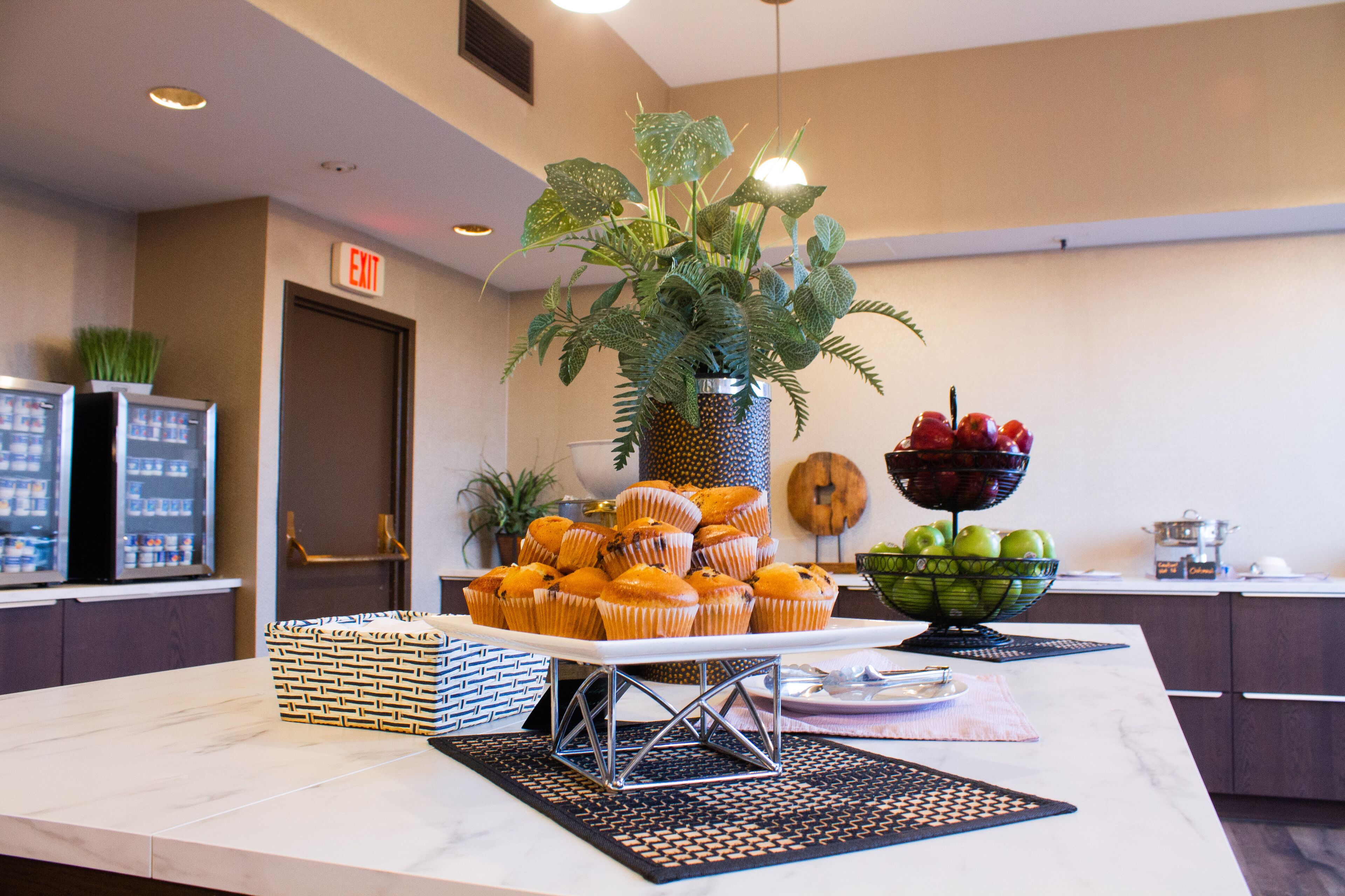 Una mesa de buffet con muffins, un bol de fruta y una planta en maceta.