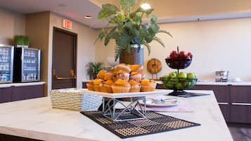 A buffet table with muffins, a fruit bowl, and a potted plant.
