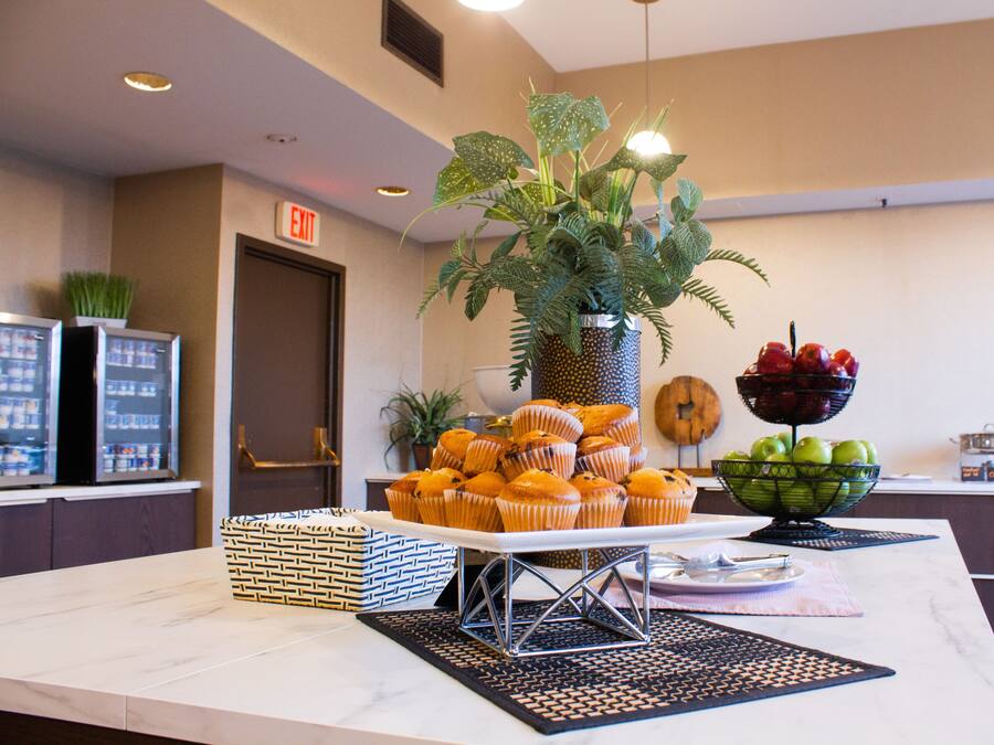 A buffet table with muffins, a fruit bowl, and a potted plant.