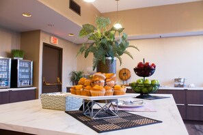 A buffet table with muffins, a fruit bowl, and a potted plant.