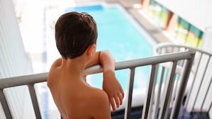 A child leaning on a balcony railing overlooking a swimming pool. - Rodd Royalty (Charlottetown)