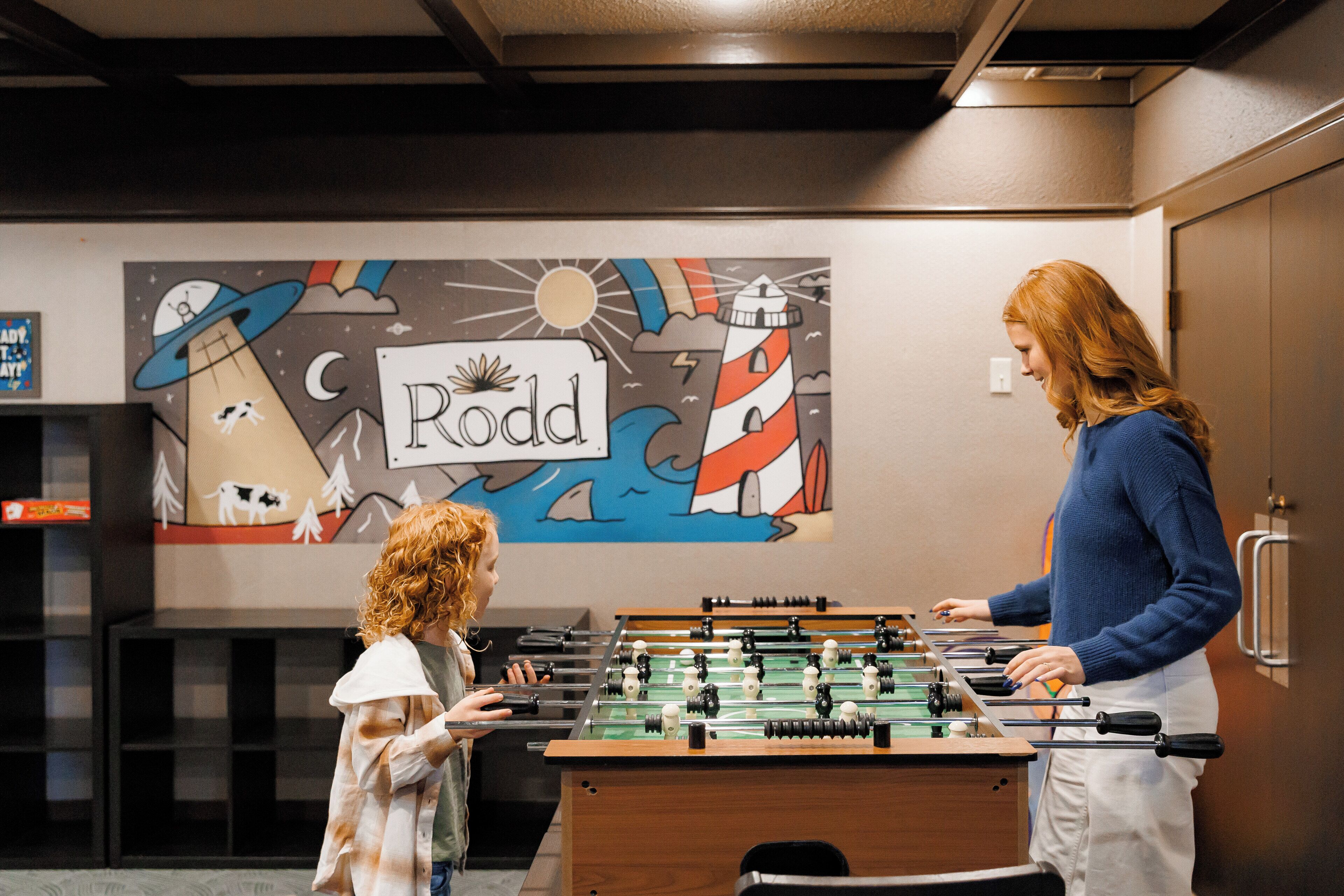 Una habitación con mesa de fútbol de mesa, un mural en la pared con un faro y un letrero que dice "Rodd".