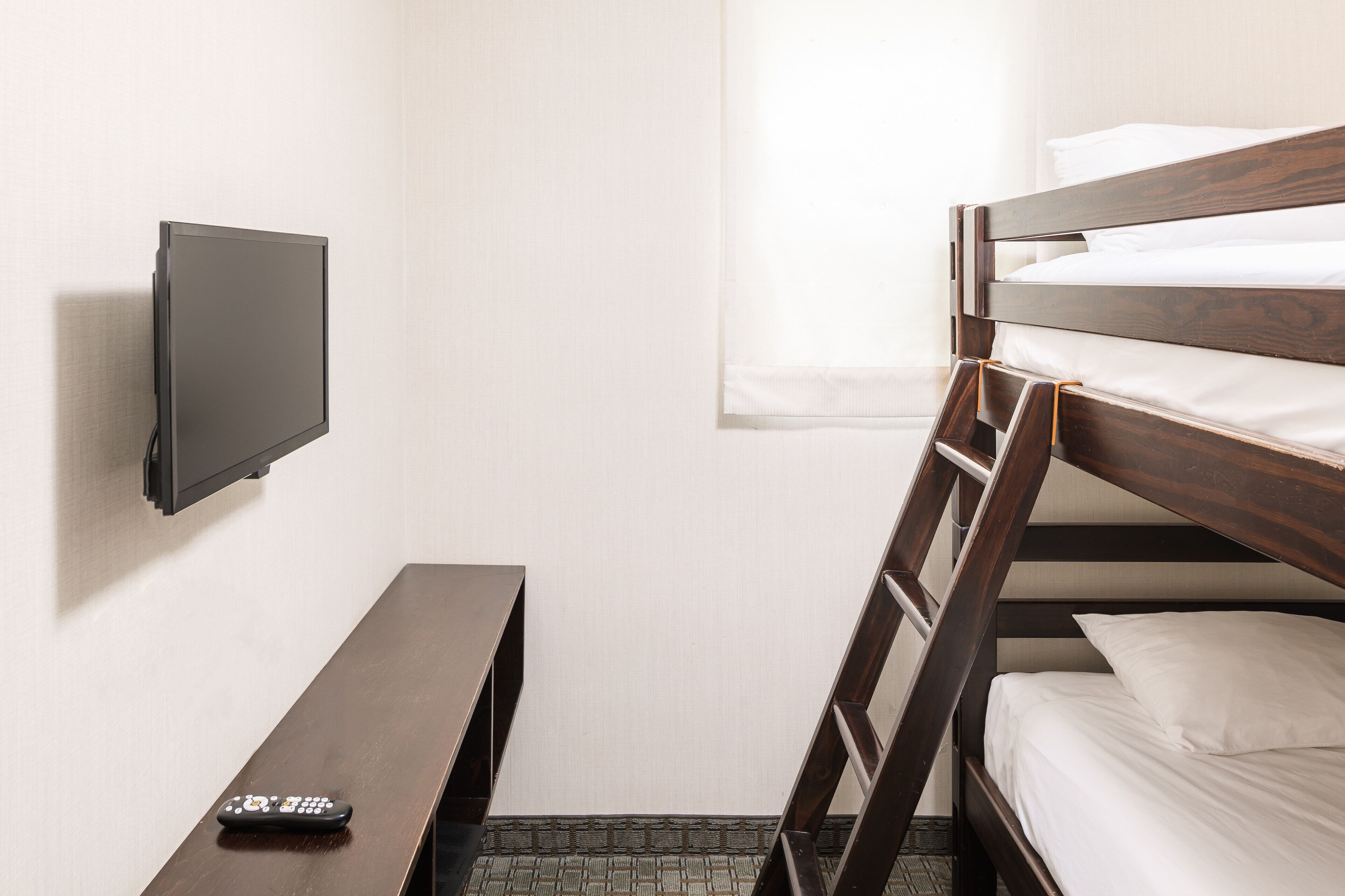 Een stapelbed met een televisie aan de muur, een klein tafeltje en een afstandsbediening op het tafeltje.