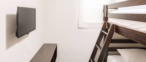 A bunk bed with a TV mounted on the wall, a small table, and a remote control on the table.