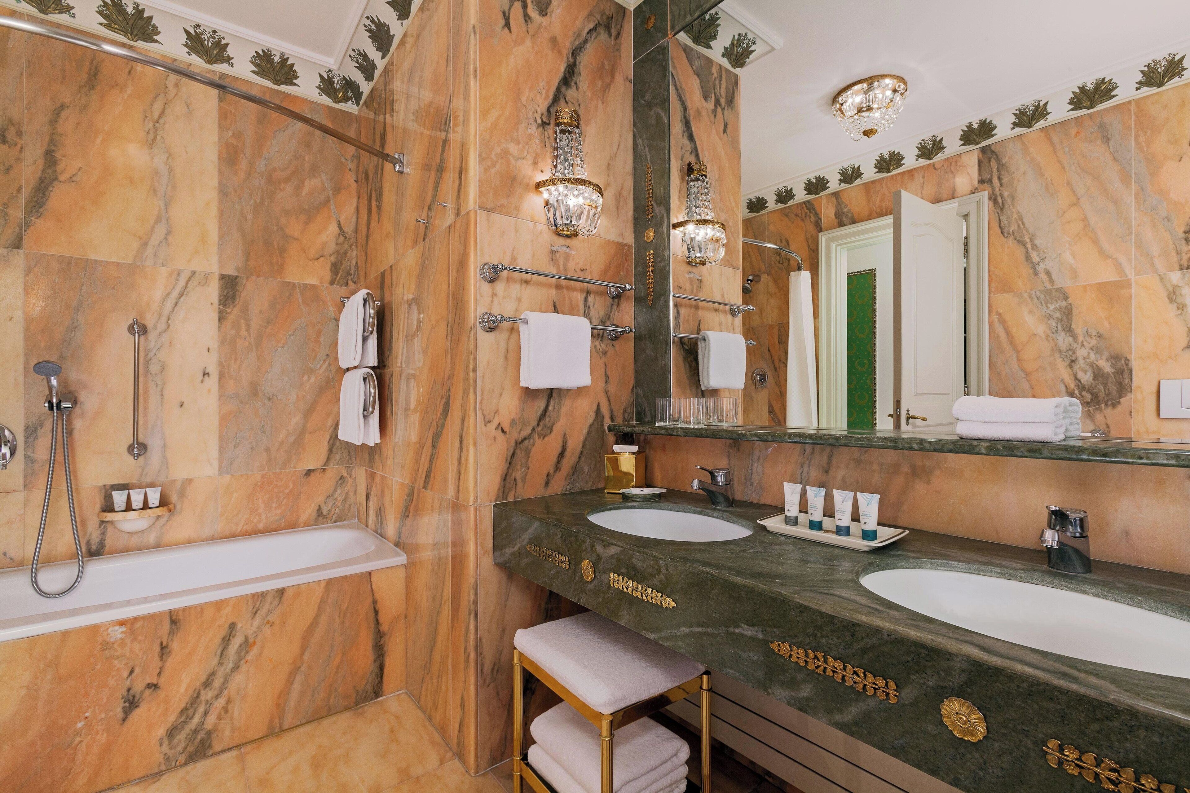 Ein luxuriöses Badezimmer mit Marmorwänden, einem großen Spiegel, zwei Waschbecken, einer Badewanne und einem Waschtisch mit Handtuchhalter.