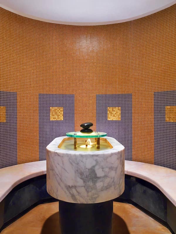 Bathroom features a central sink, curved basin, and mosaic tile walls.