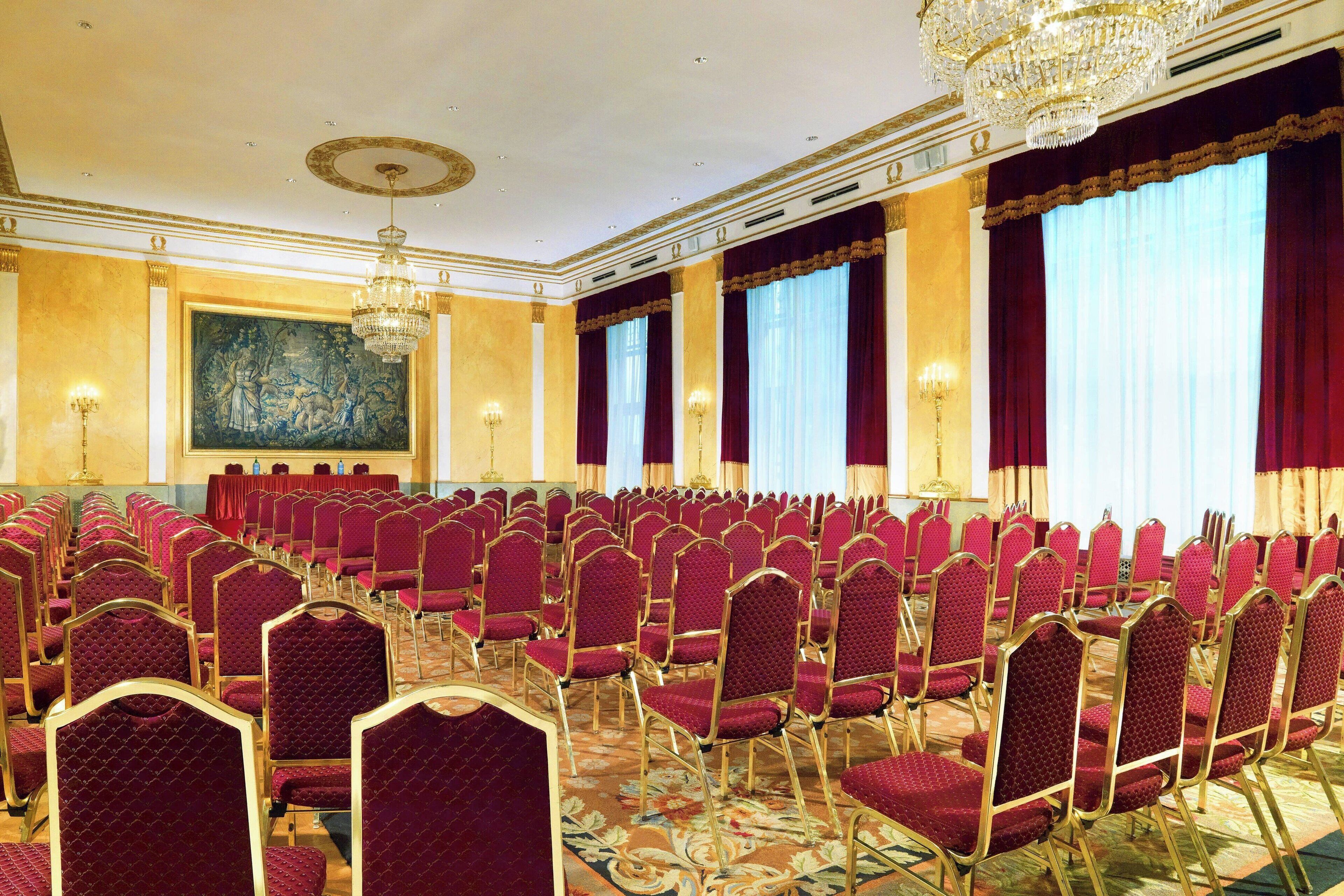 A conference room with rows of red chairs, a large chandelier, and a mural on the wall.