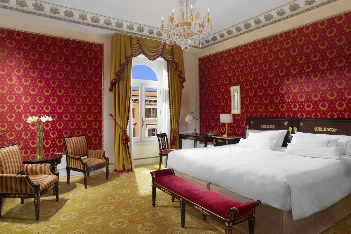 A hotel room with a large bed, two armchairs, a bench, a table, and a desk.