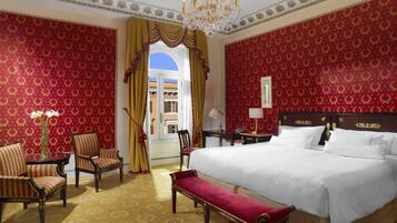 Ein Hotelzimmer mit einem großen Bett, zwei Sesseln, einer Bank, einem Tisch und einem Schreibtisch.