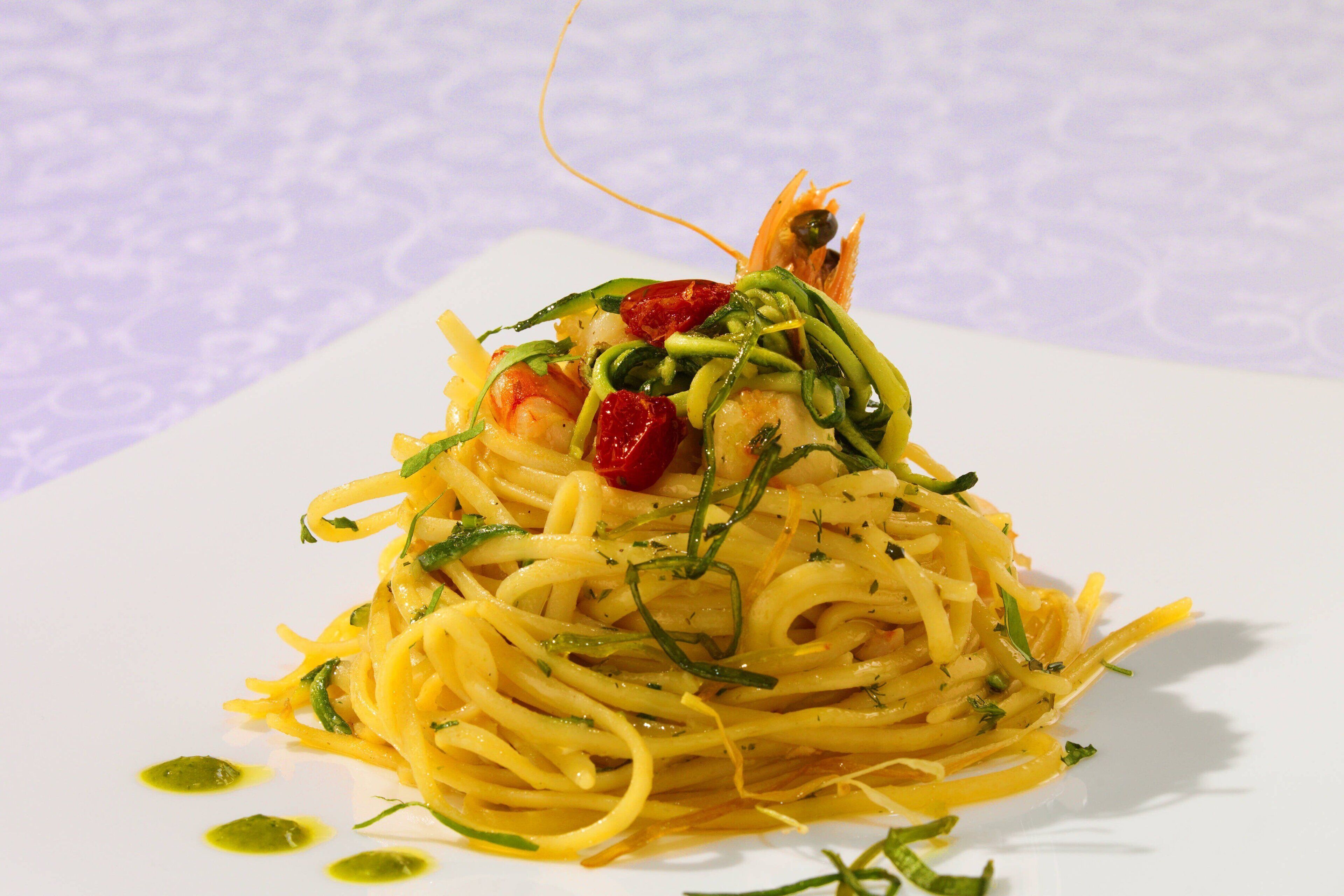 A plate of spaghetti with shrimp, garnished with herbs and lemon zest.
